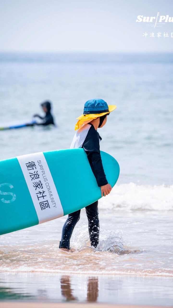 孩子抱着冲浪板走向海边，准备第一次冲浪体验